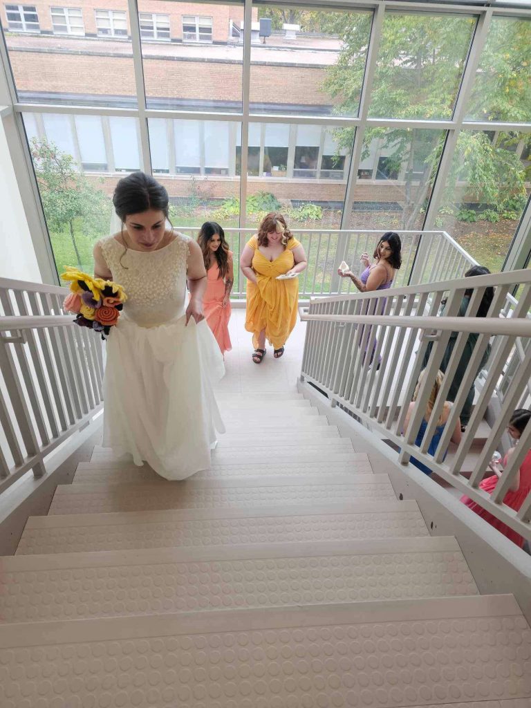 Bride and bridesmaids make their way up the light filled stairway at UW Stevens Point.
