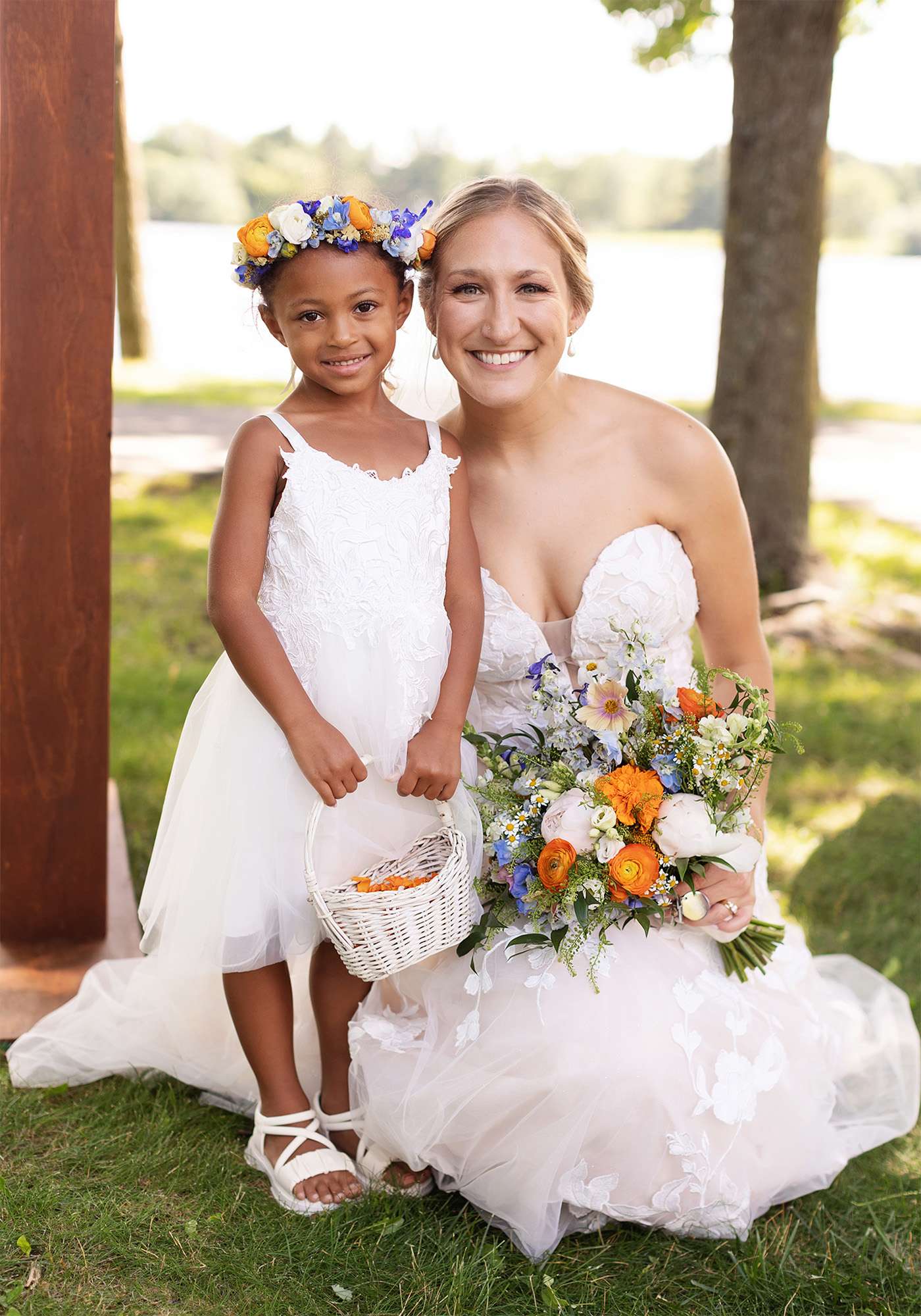 Bride with vibrant floral bouquet poses with flower girl wearing a floral wreath in her hair.