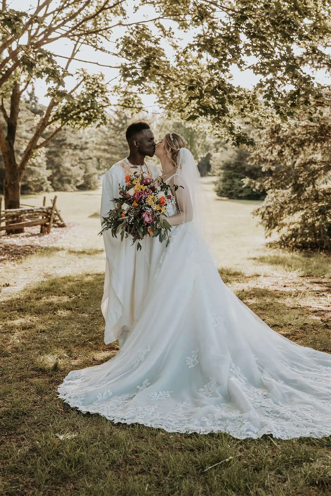 Bride and groom sharing a first kiss outdoors surrounded by lush green trees, bouquet by Archer and Bliss Floral, Wisconsin summer wedding.