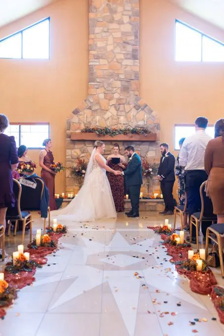 Wedding ceremony in front of stone fireplace with candles and fall aisle décor at Tundra Lodge Resort & Conference Center.
