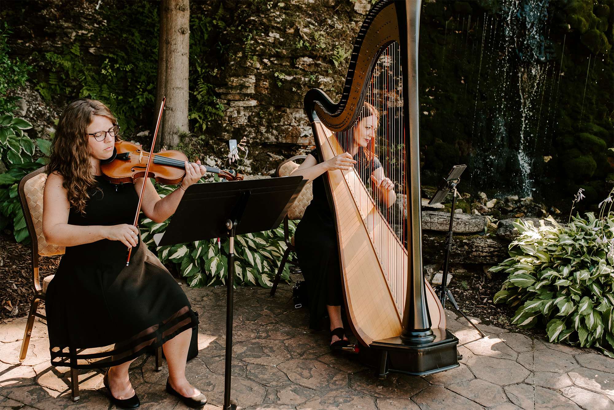 Harpist and violinist perform at outdoor wedding ceremony.