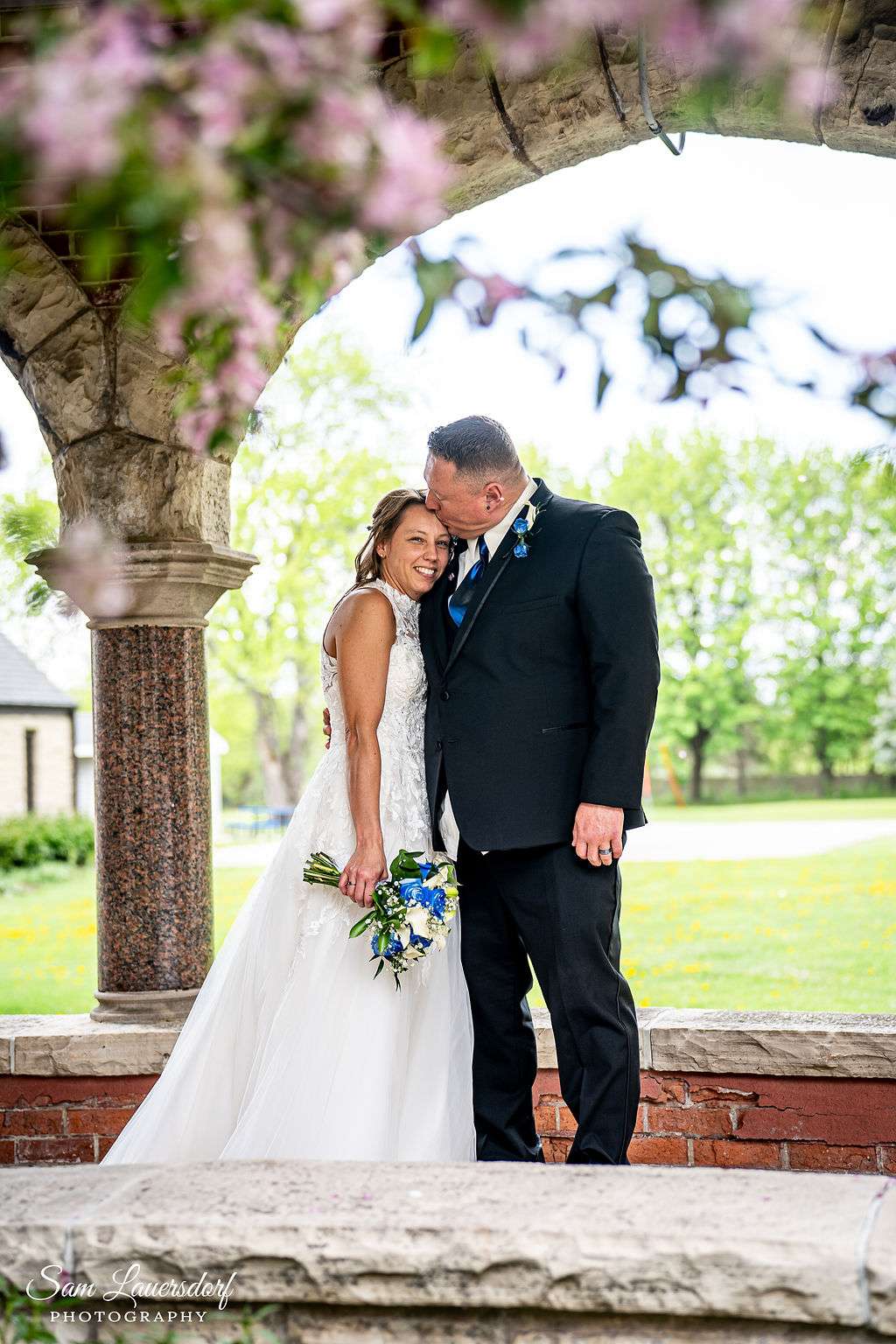 Groom kisses bride on forehead.