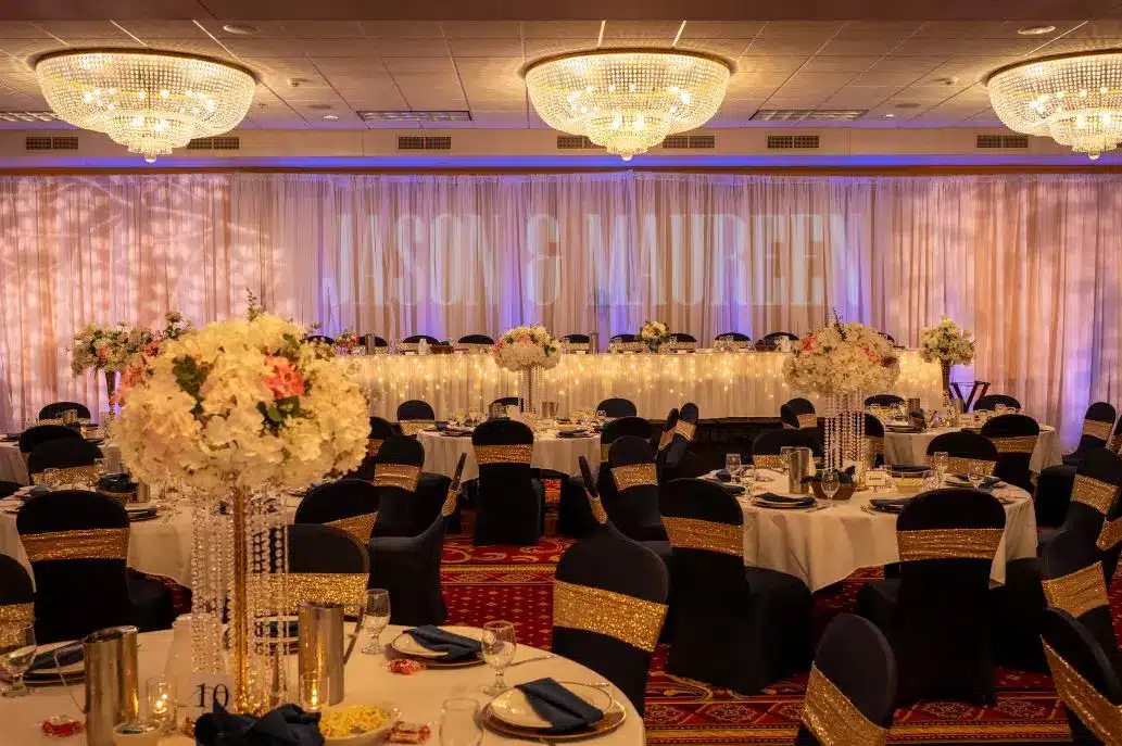 Ballroom wedding at Tundra Lodge Resort with draped backdrop, illuminated head table, and navy chairs accented with gold sashes.