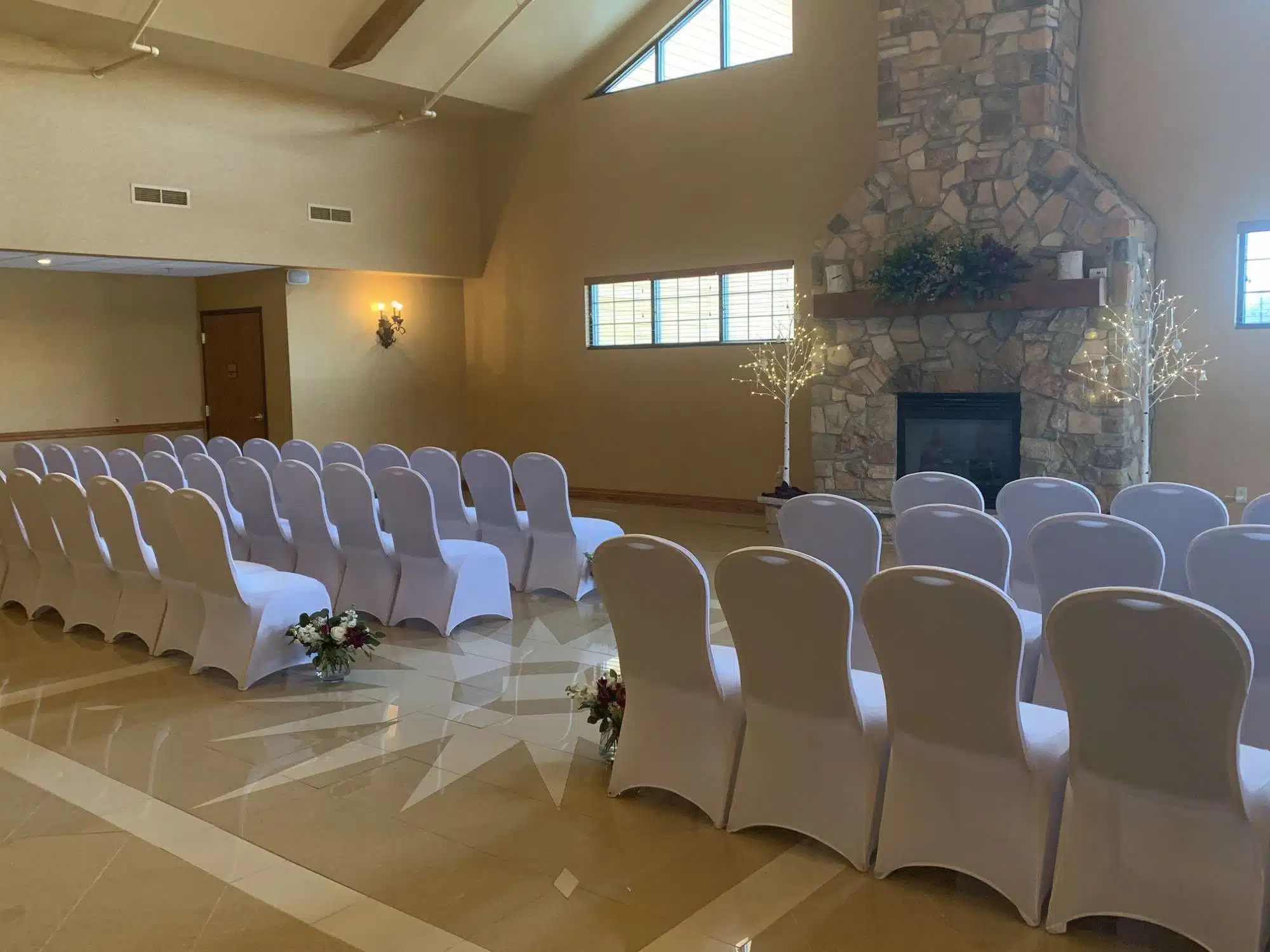 Indoor wedding ceremony setup with white chairs and 45-foot stone fireplace at Tundra Lodge Resort & Conference Center