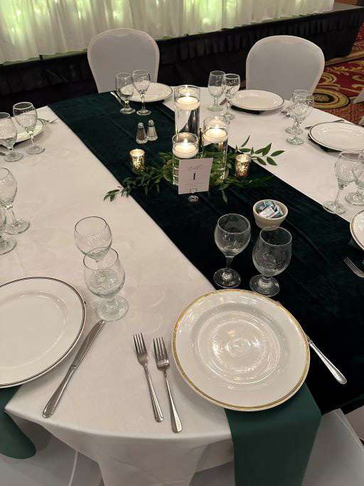 Wedding reception table with candle centerpiece, greenery, and dark green runner