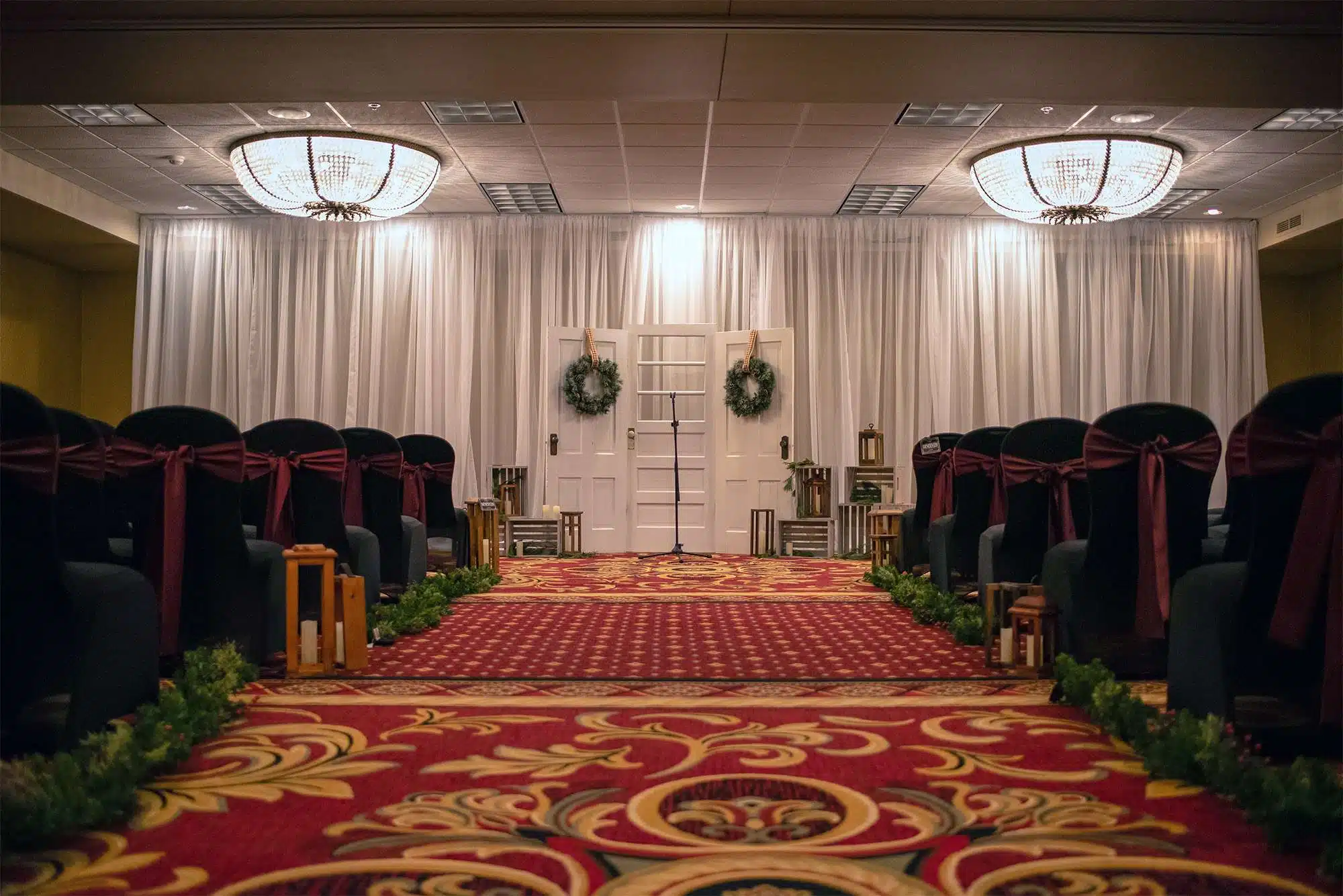 Indoor wedding ceremony aisle with draped backdrop, white doors, and lantern décor at Tundra Lodge Resort & Conference Center.