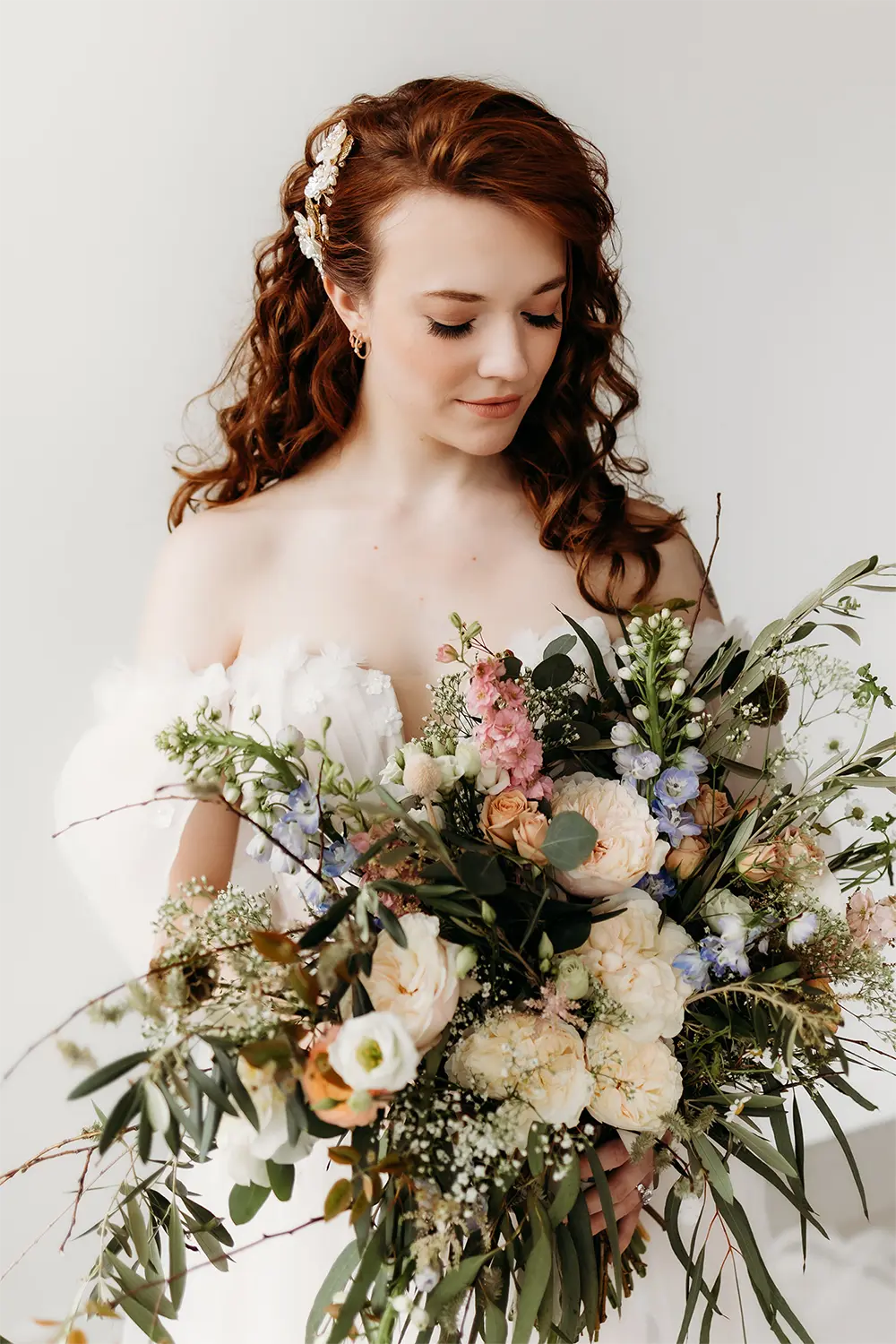 Romantic Garden-Style Bridal Bouquet. Bride with red hair holding a soft, garden-style bouquet with blush, peach, and blue flowers.