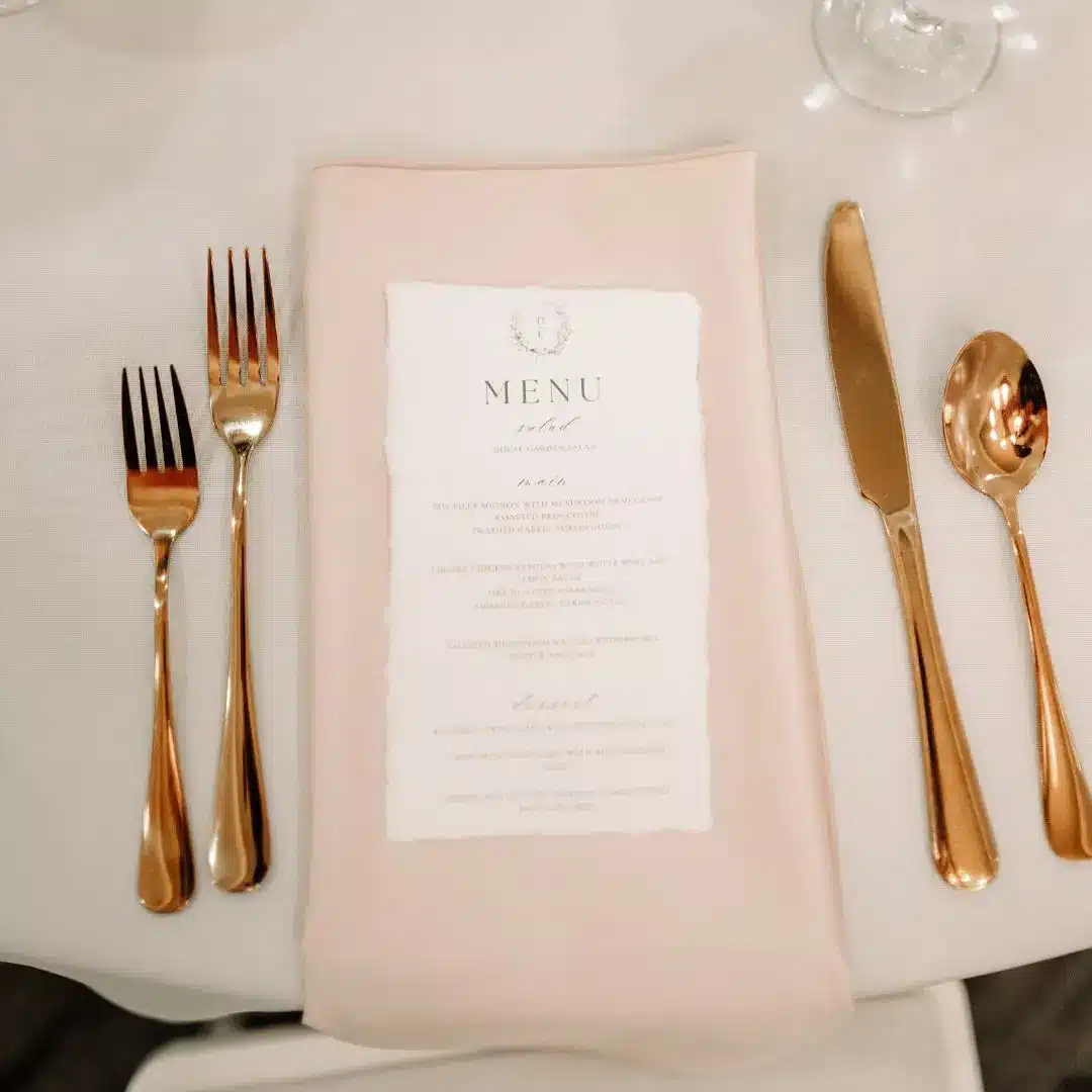 Dinner menu on top of pale pink napkin and gold flatware by I Do Decorating & Rental Service