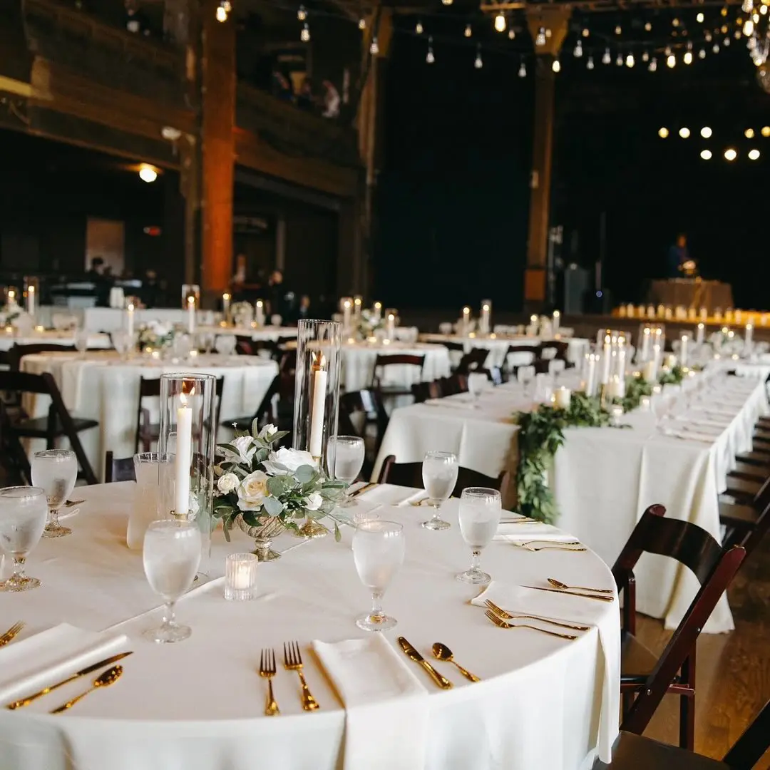 reception tables set in white linens, floral centerpiece and candles with gold flatware by I Do Decorating & Rental Service