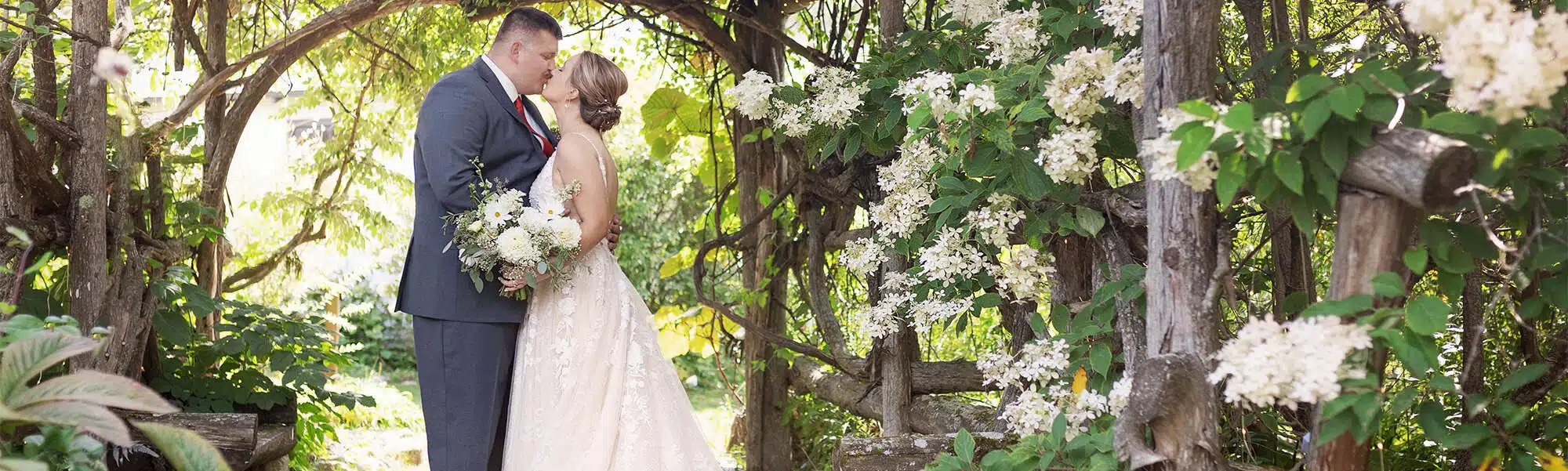 couple sharing a kiss under branched archway amid natural greenery at The Grain Loft