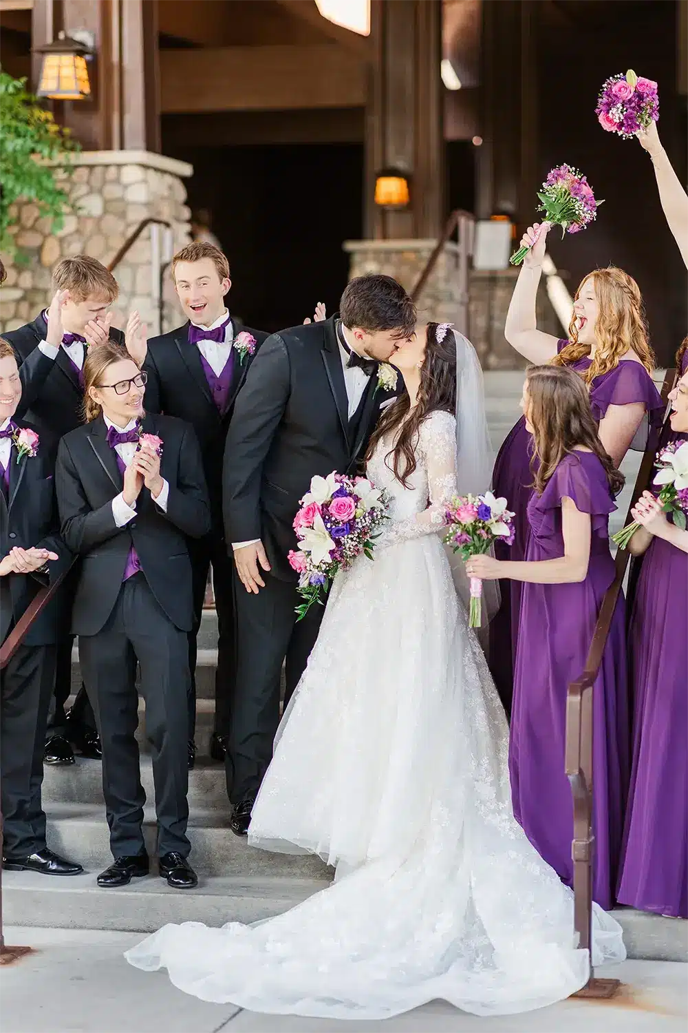 Groom kisses bride as wedding party cheers. Groom kisses bride as wedding party cheers.