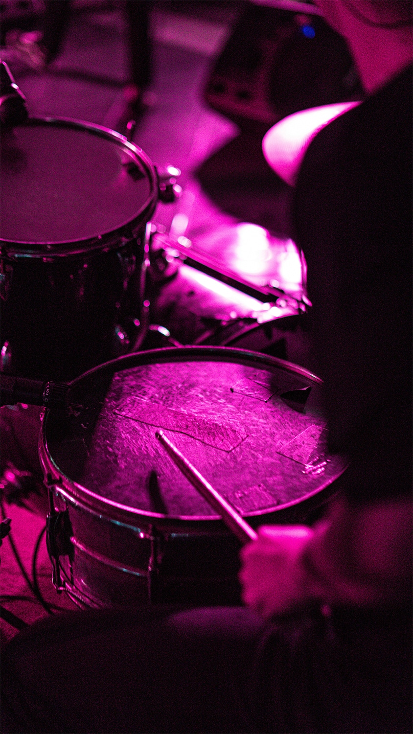 Person playing drums in violet lighting. Person playing drums in violet lighting.