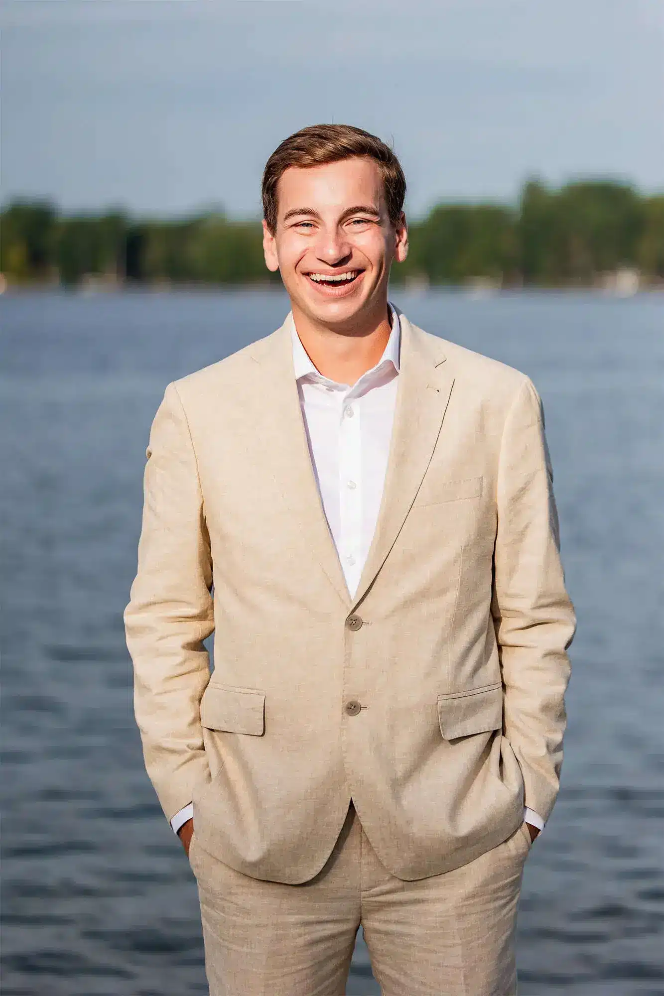 Clintonville-lakeside-wedding-reception-25 Groom in tan linen look tux standing with hands in pocket on pier