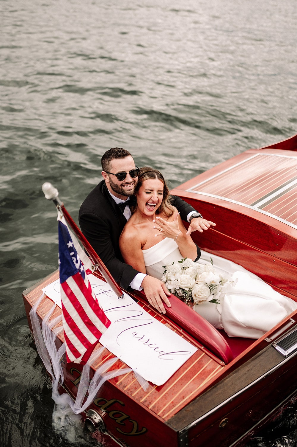 Bride and groom pose in a classic wooden boat with “Just Married” sign on it. Bride and groom pose in a classic wooden boat with "Just Married" sign on it.