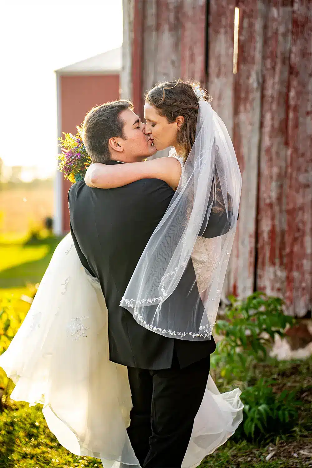 Woelfel Homestead bride and groom. Bride in veil kisses groom as he holds her at Woelfel Homestead wedding.
