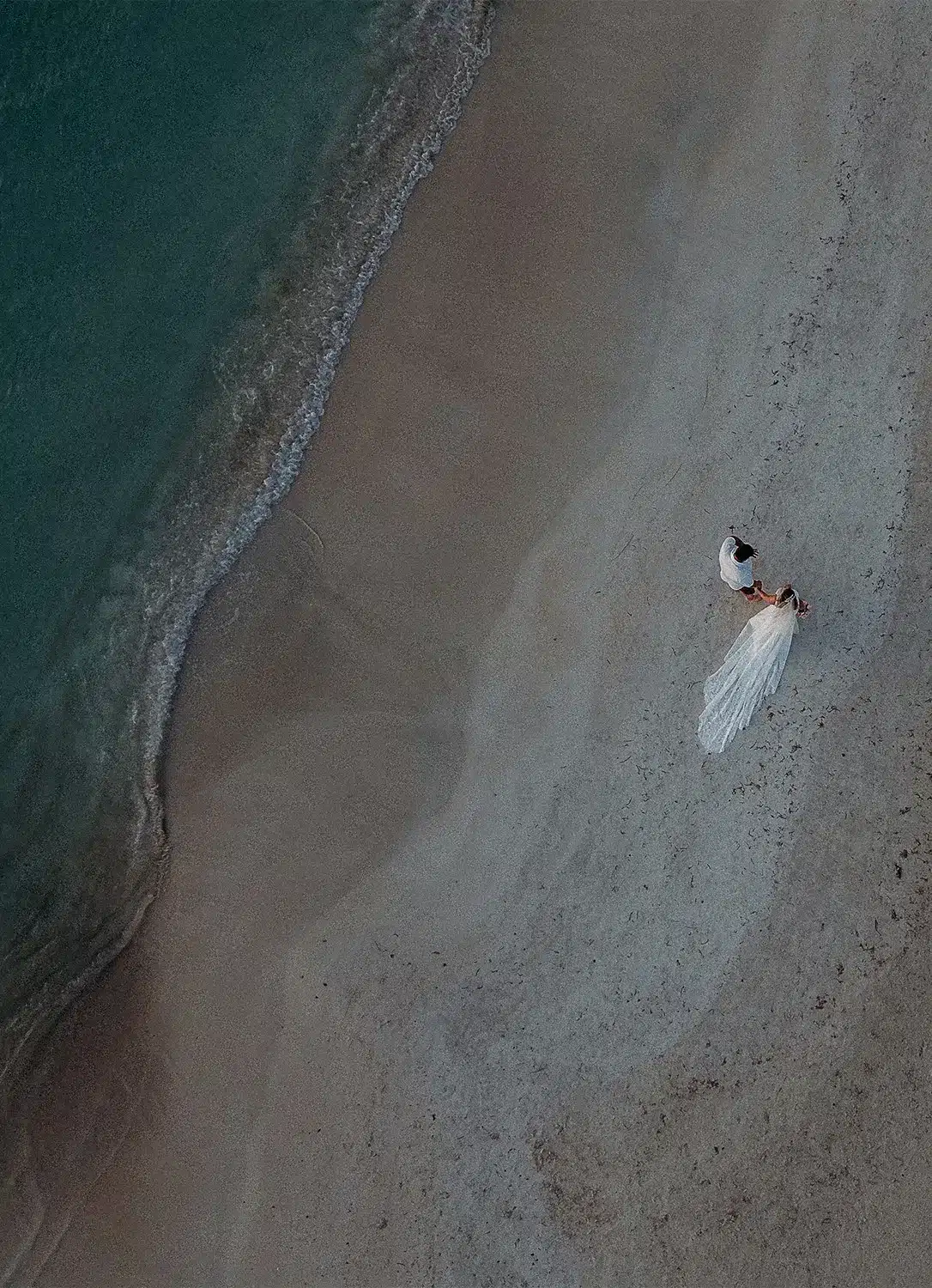 Drone image of couple walking on beach. Drone image of couple walking on beach.