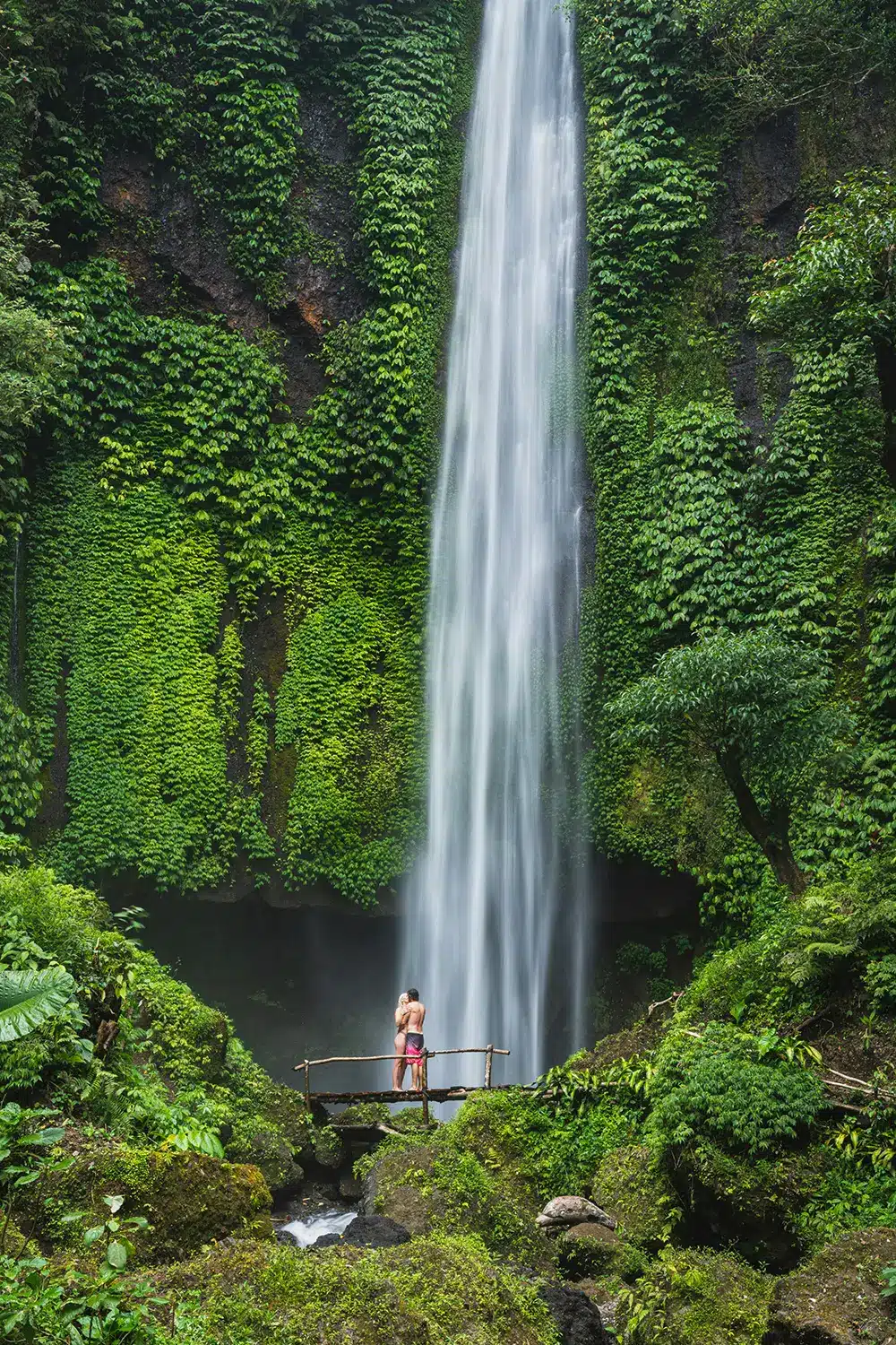 Couple hug on bridge near waterfall surrounded by greenery. Couple hug on bridge near waterfall surrounded by greenery.