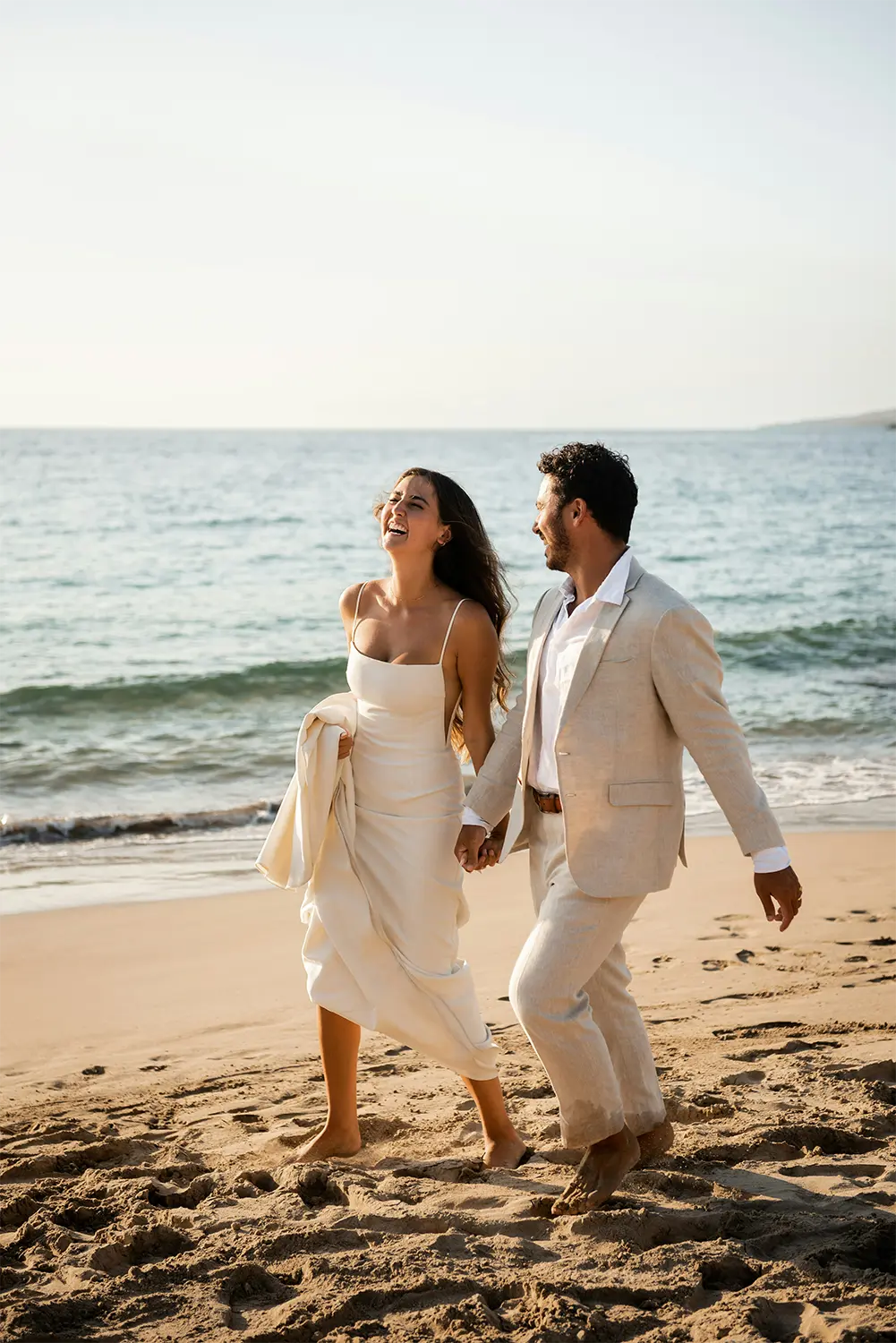 Destination wedding newlyweds walk laughing on the beach. Destination wedding newlyweds walk laughing on the beach.