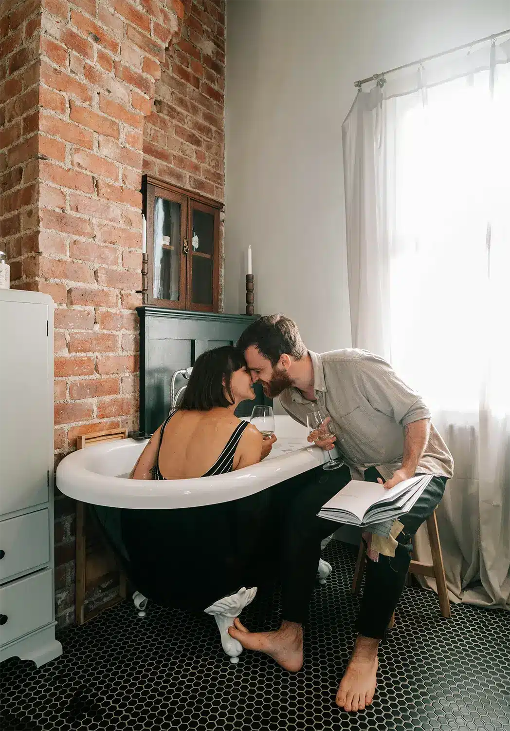 Woman in bathtub kisses man who is reading to her while they drink wine. Woman in bathtub kisses man who is reading to her while they drink wine.