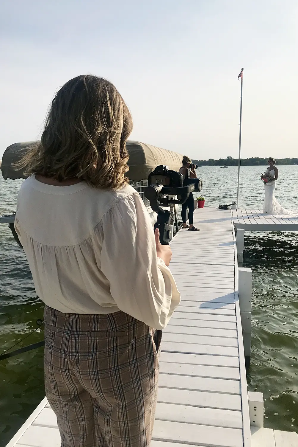 Wedding filmmaker working on pier with bride. Wedding filmmaker working on pier with bride.