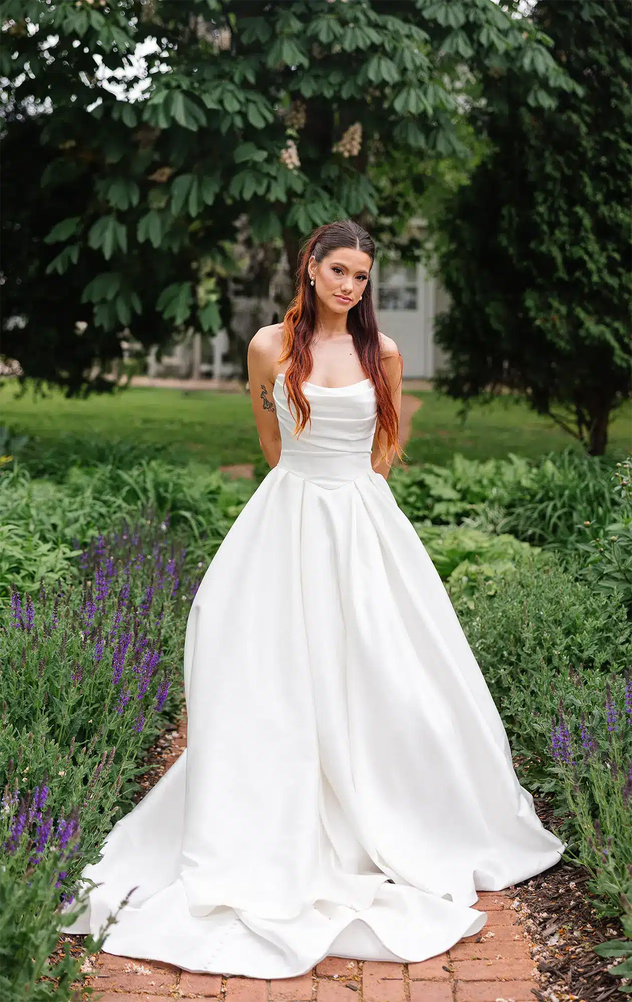 Bride in strapless white ballgown stands on garden path at Heritage Hill in Green Bay. Bride in strapless white ballgown stands on garden path at Heritage Hill in Green Bay.