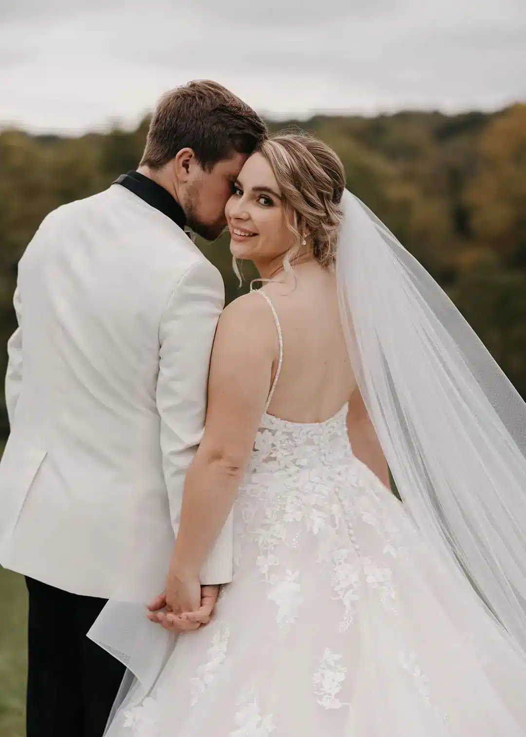Bride in veil looks over her shoulder with groom by her side.