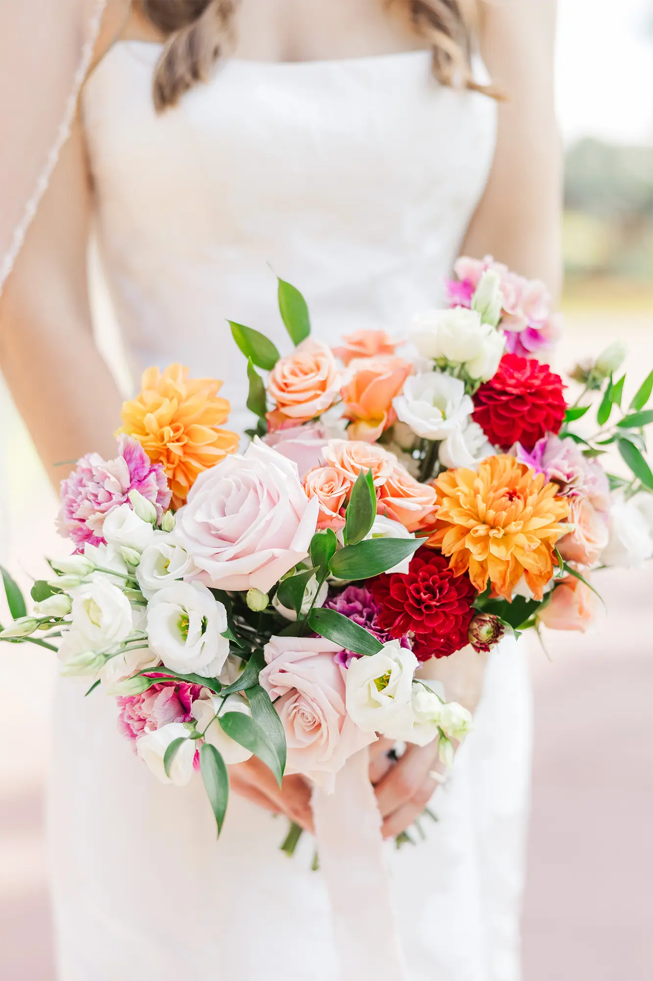 Bride holding a colorful garden-style wedding bouquet with peach, coral, and white flowers.