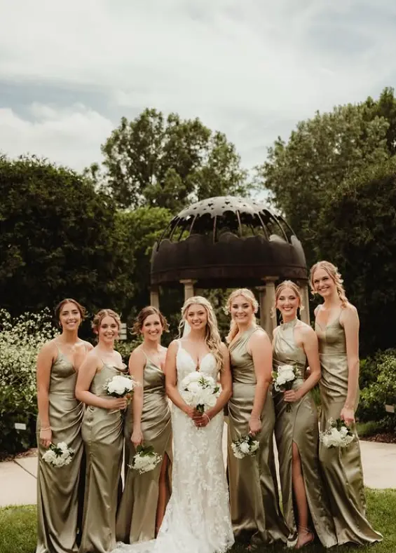Bride with bridesmaids in sage green dresses holding white bouquets at Green Bay Botanical Garden.