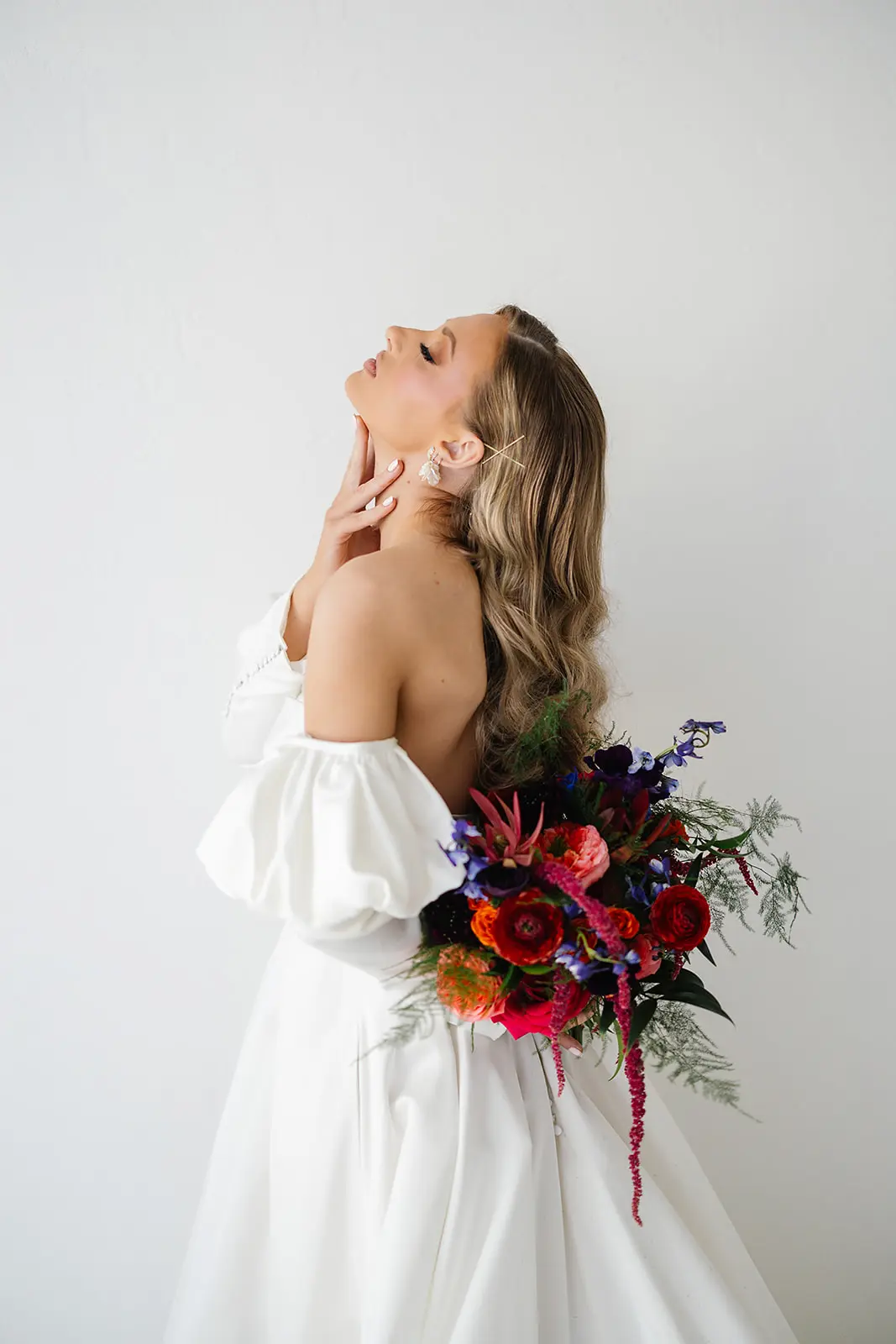 Bride in off-the-shoulder gown holding a vibrant, colorful bouquet with bold red and orange flowers.
