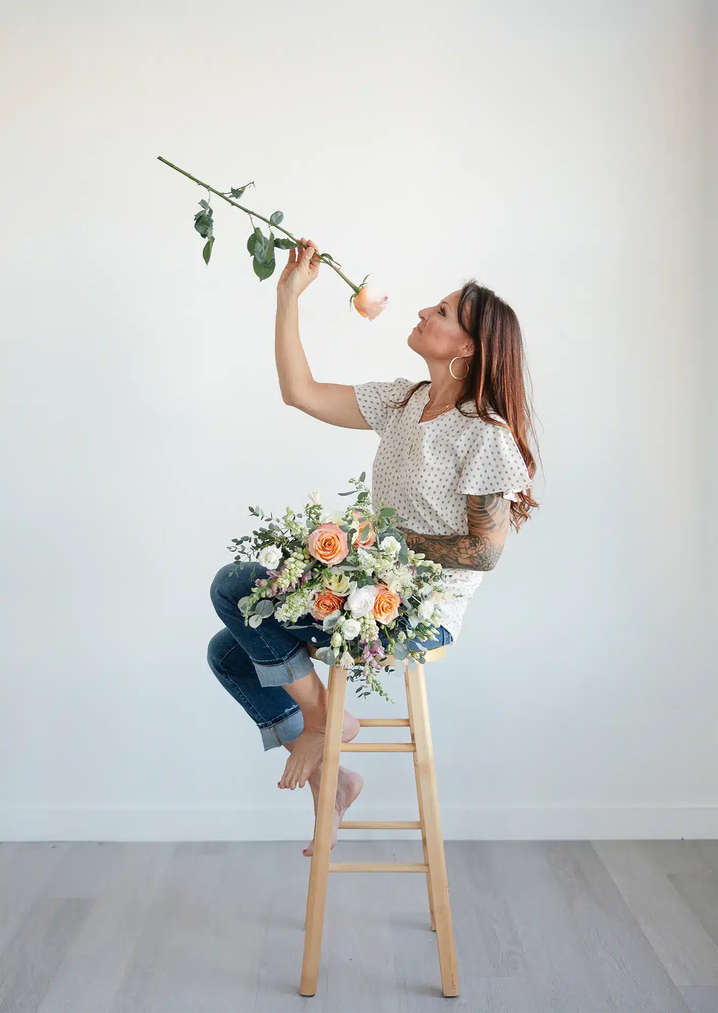 Katie, owner of Archer & Bliss Floral, holding a single peach rose while seated with a garden-style bouquet.