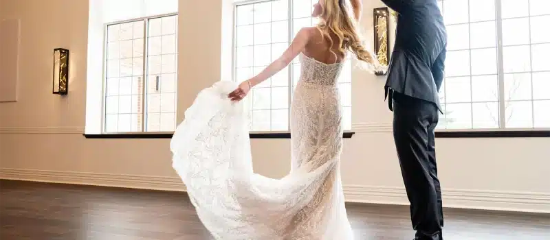 Bride twirling in lace wedding dress with groom in front of large windows at Stonewood Venue