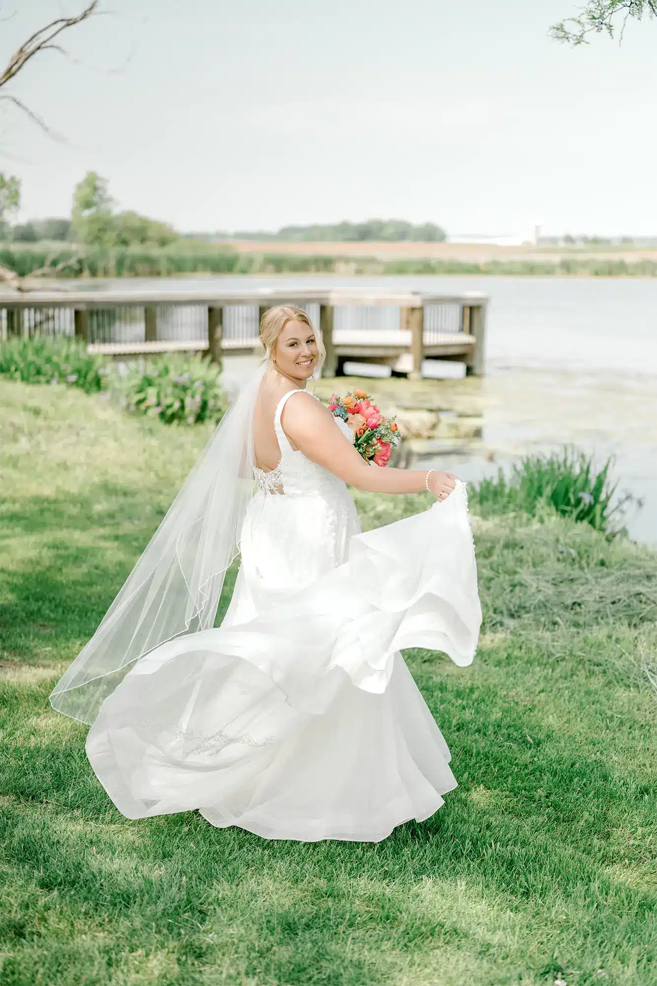 Bride Portrait by the Water Bride twirling in wedding dress by lakeside holding colorful bouquet.