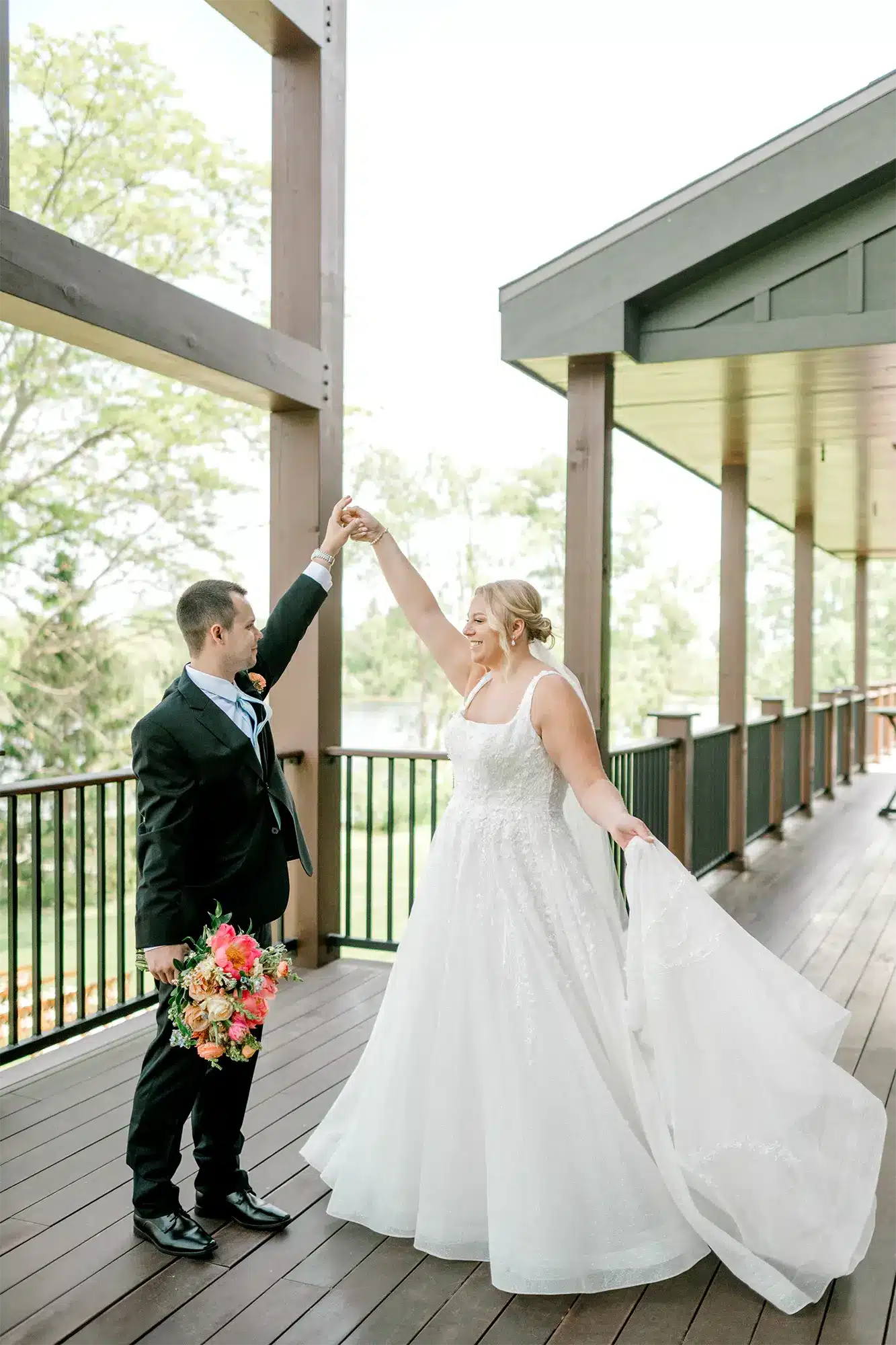 Couple Portrait on the Porch Bride twirling under groom’s arm on outdoor porch holding bouquet.