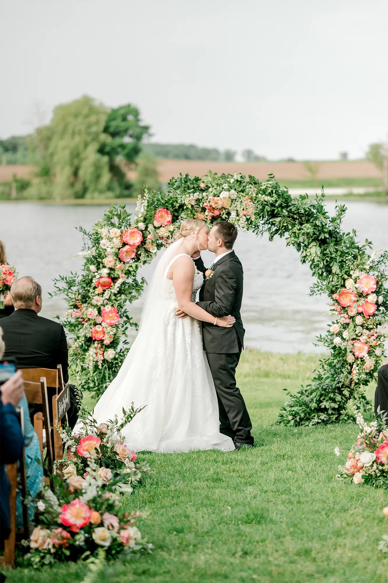 Lakeside Ceremony Kiss at Round Lake Farms. Bride and groom kissing under floral arch at lakeside ceremony at Round Lake Farms.