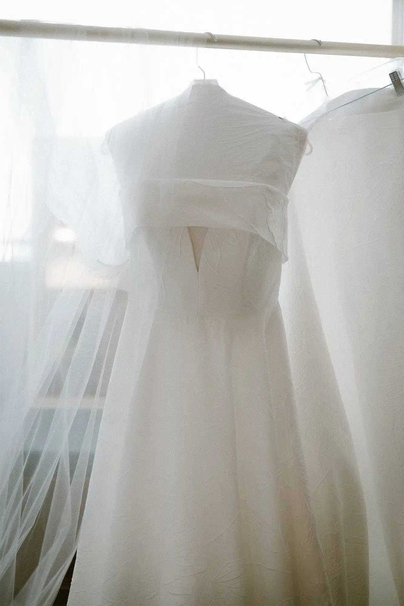 Bridal Gown Hanging in Soft Window Light Wedding dress hanging in window with soft natural light bridal detail Heidel House Green Lake Wisconsin.