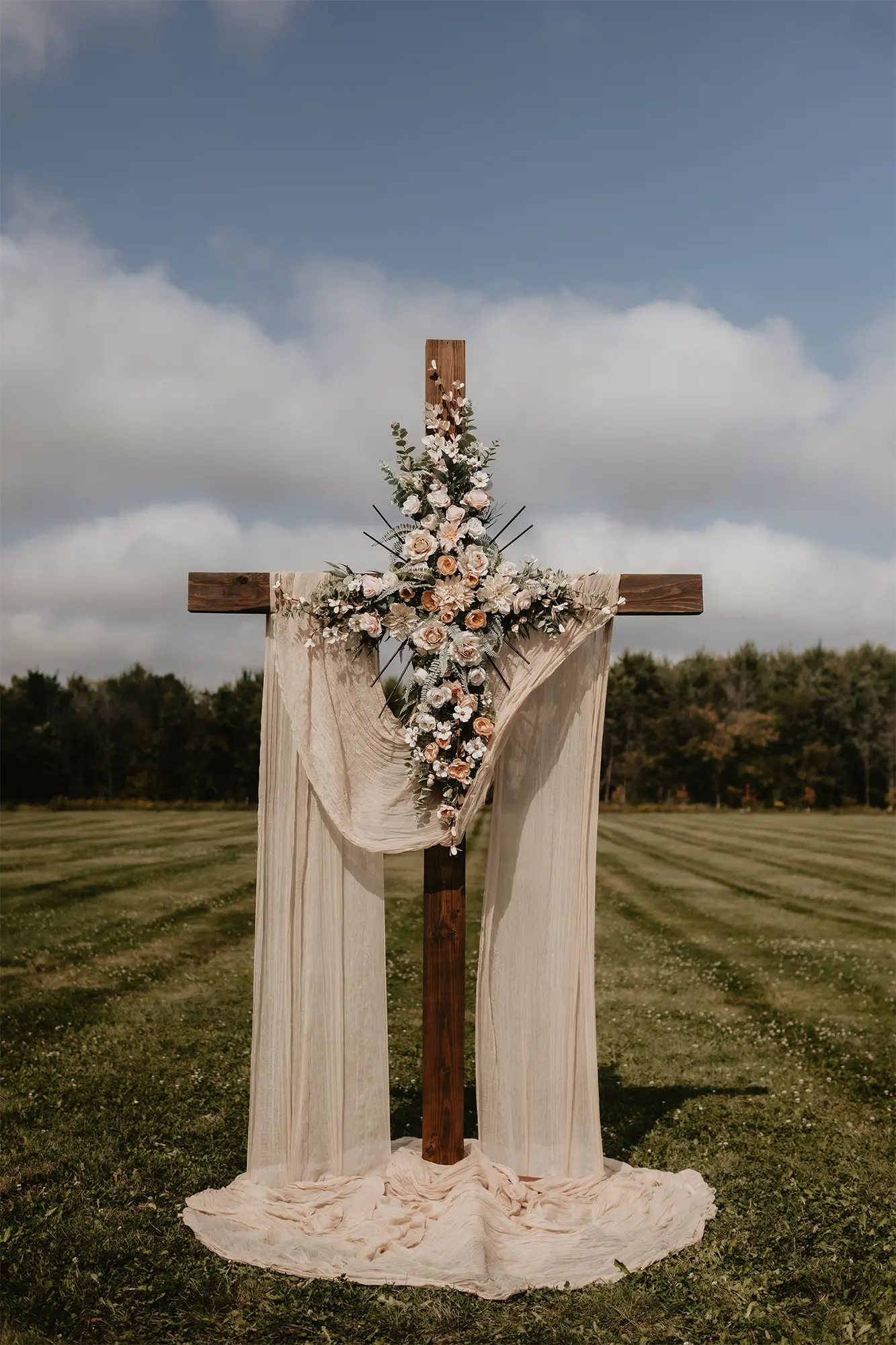Ceremony Cross with Draped Fabric and Florals at Stone Prairie Outdoor wedding ceremony cross with draped fabric and blush floral arrangement at Stone Prairie Wisconsin