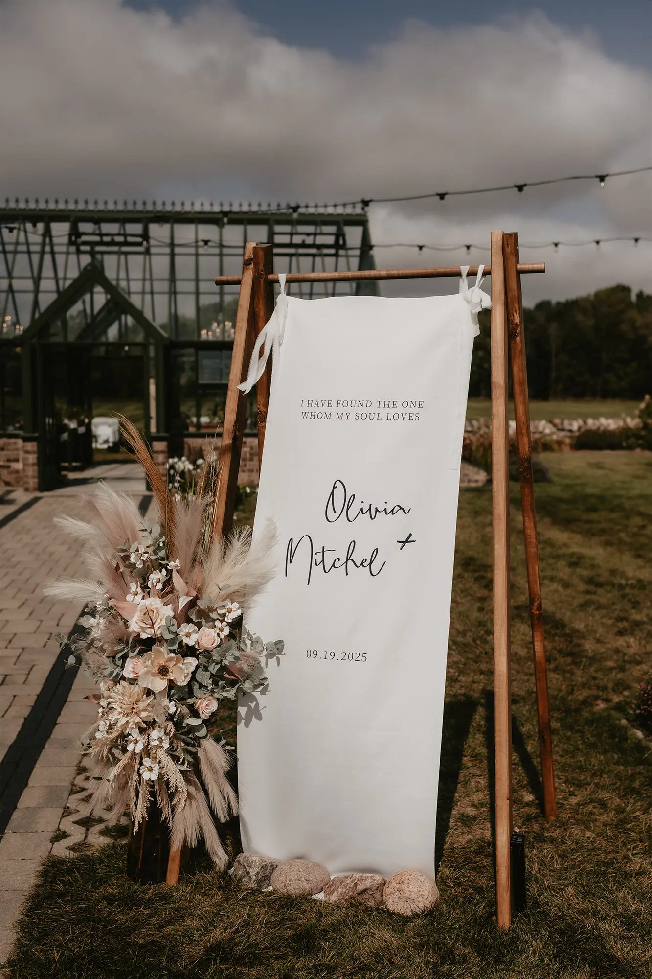 Western Elegance Wedding Welcome Sign at Stone Prairie Custom wedding welcome sign with “Olivia + Mitchel” displayed on fabric banner with pampas grass florals at Stone Prairie greenhouse venue in Brillion Wisconsin